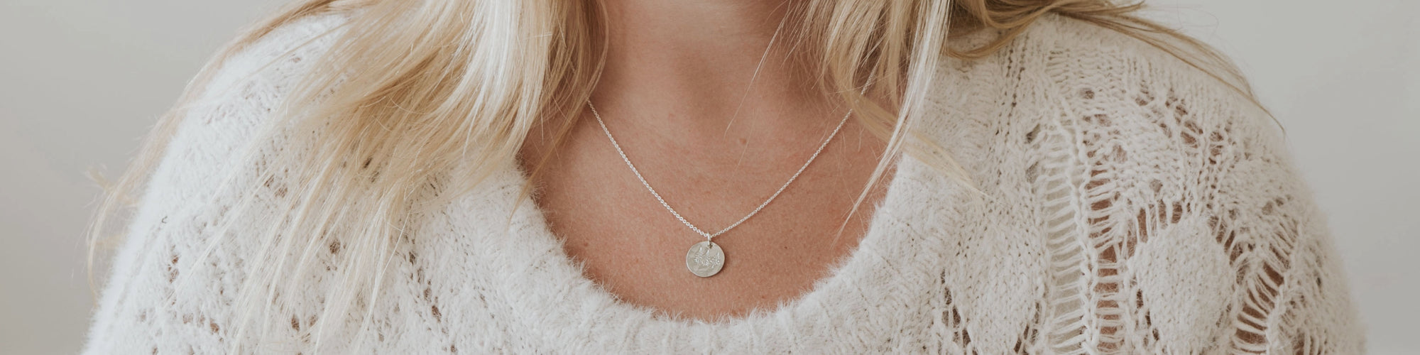 Close-up of a woman wearing a white tank top and a delicate necklace with a small pendant.
