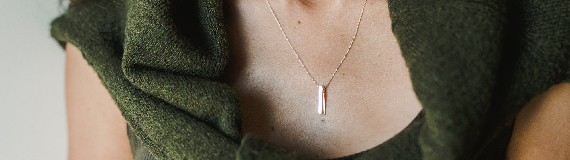 A close-up view of a person wearing a simple bar pendant necklace.