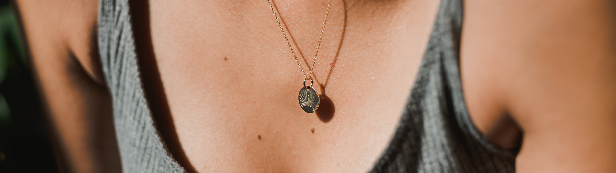 Close-up of a necklace with a small, oval pendant on a woman wearing a gray tank top, focused on the chest area with a blurred background.