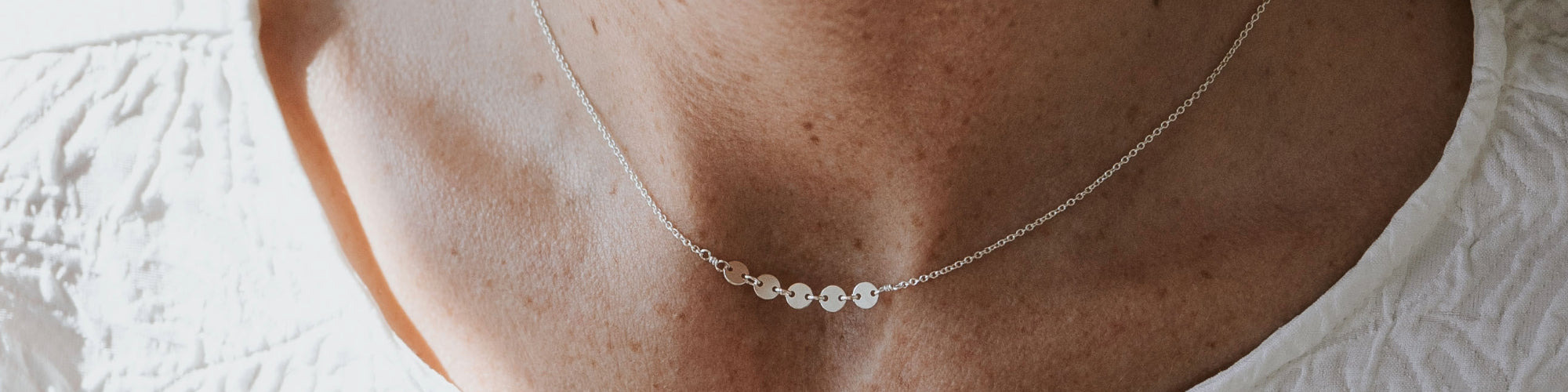 Close-up of a person wearing a white v-neck shirt with a silver necklace featuring a round pendant that says "mama.