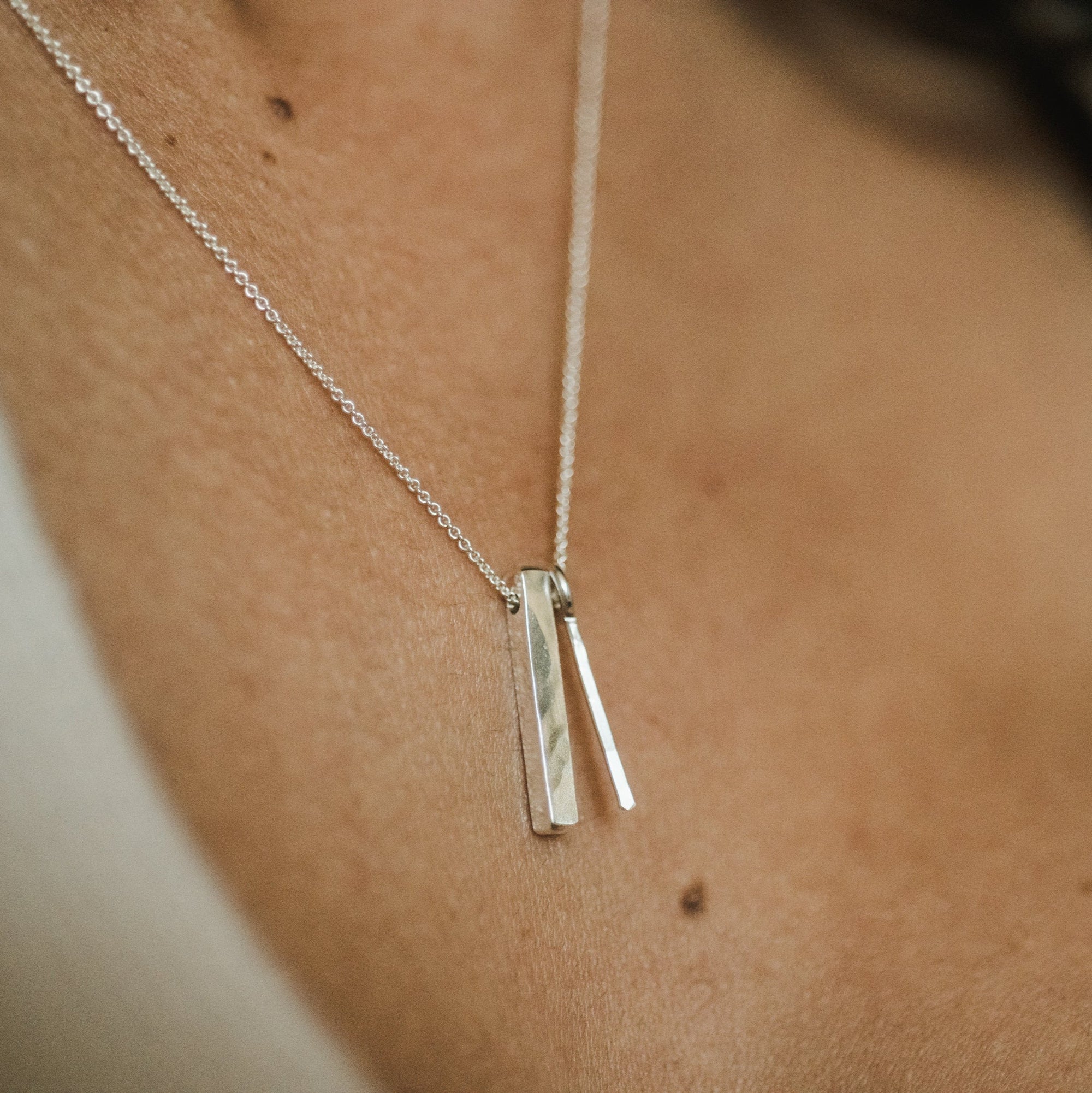 A close-up of a person's neck wearing the top-selling Through Thick & Thin Necklace from Becoming Jewelry, adorned with two slim rectangular pendants.