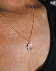Close-up of a person wearing the gold River Necklace by Becoming Jewelry, showcasing a round pendant adorned with a leaf pattern, symbolizing the indomitable spirit of remarkable women.