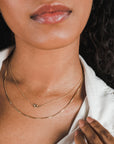 Close-up of a woman with curly hair wearing a white blouse and a delicate sterling silver Becoming Jewelry box chain necklace.