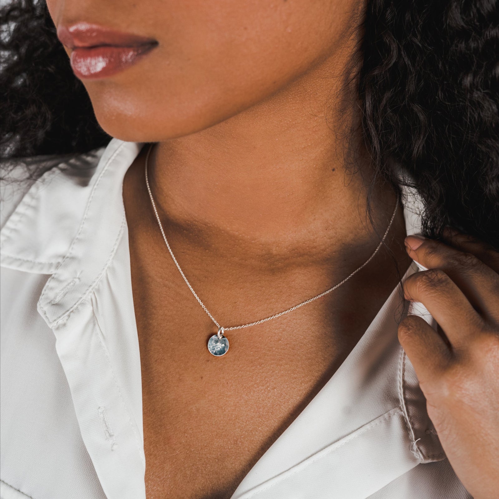A woman with curly hair wearing a white shirt and a Becoming Jewelry sterling silver Believe in Magic Necklace with a blue pendant.