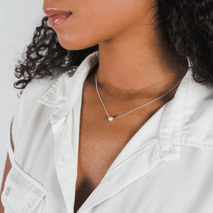 A woman wearing a white blouse and a delicate Becoming Jewelry Simplify Necklace.