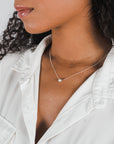 A woman wearing a white blouse and a delicate Becoming Jewelry Simplify Necklace.