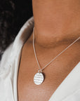 Close-up of a woman wearing a Becoming Jewelry Strong Women Necklace with a round pendant inscribed with text.