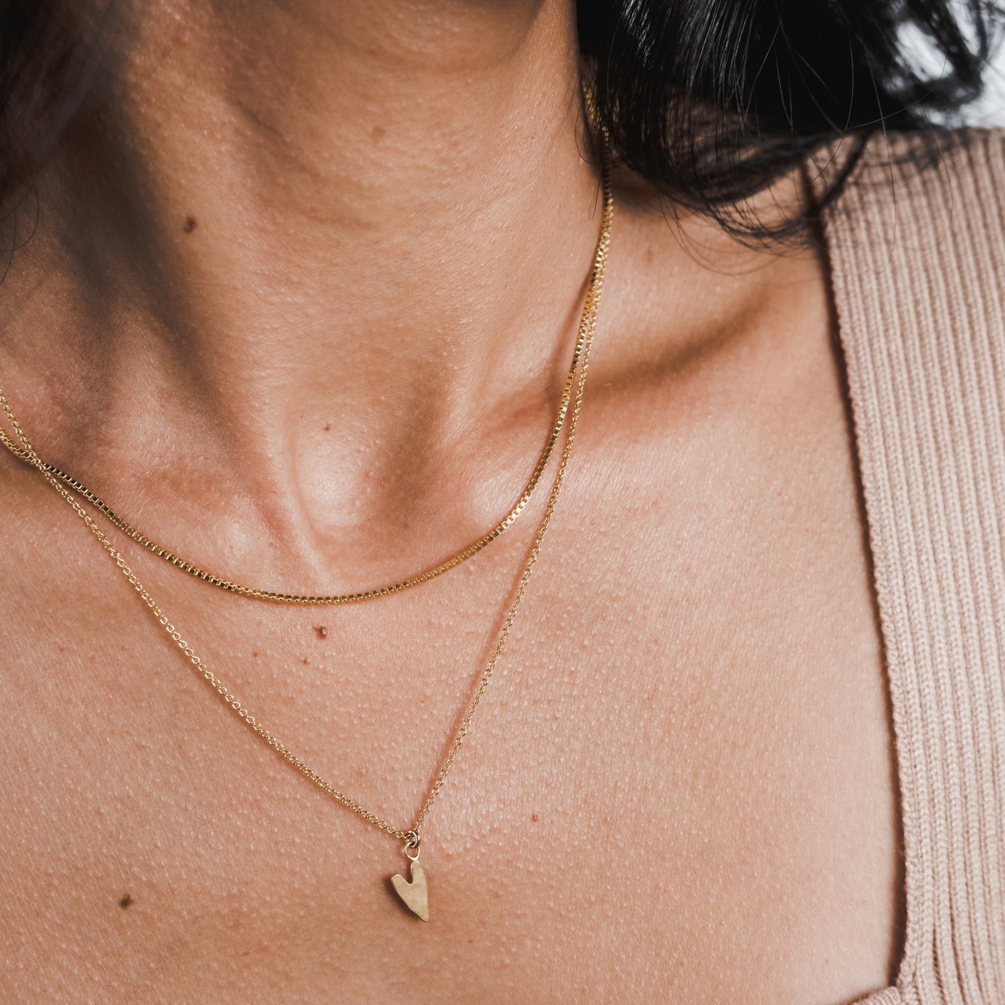 A close-up of a woman&#39;s neck wearing a Becoming Jewelry box chain necklace with a heart pendant.