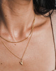 A close-up of a woman's neck wearing a Becoming Jewelry box chain necklace with a heart pendant.