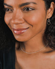 A woman with curly hair is smiling and wearing silver hoop earrings and a delicate Becoming Jewelry Figaro Chain Necklace. She is dressed in a black top, achieving a layered look.