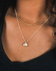 A person wearing a black V-neck shirt and the Count My Blessings Necklace from Becoming Jewelry, along with another gold necklace featuring a round pendant, exudes elegance. The accessories would make a charming gift for any occasion.