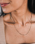 Close-up of a person wearing Becoming Jewelry's Figaro Chain Necklace, a delicate double gold chain that perfectly complements their sleeveless beige top.