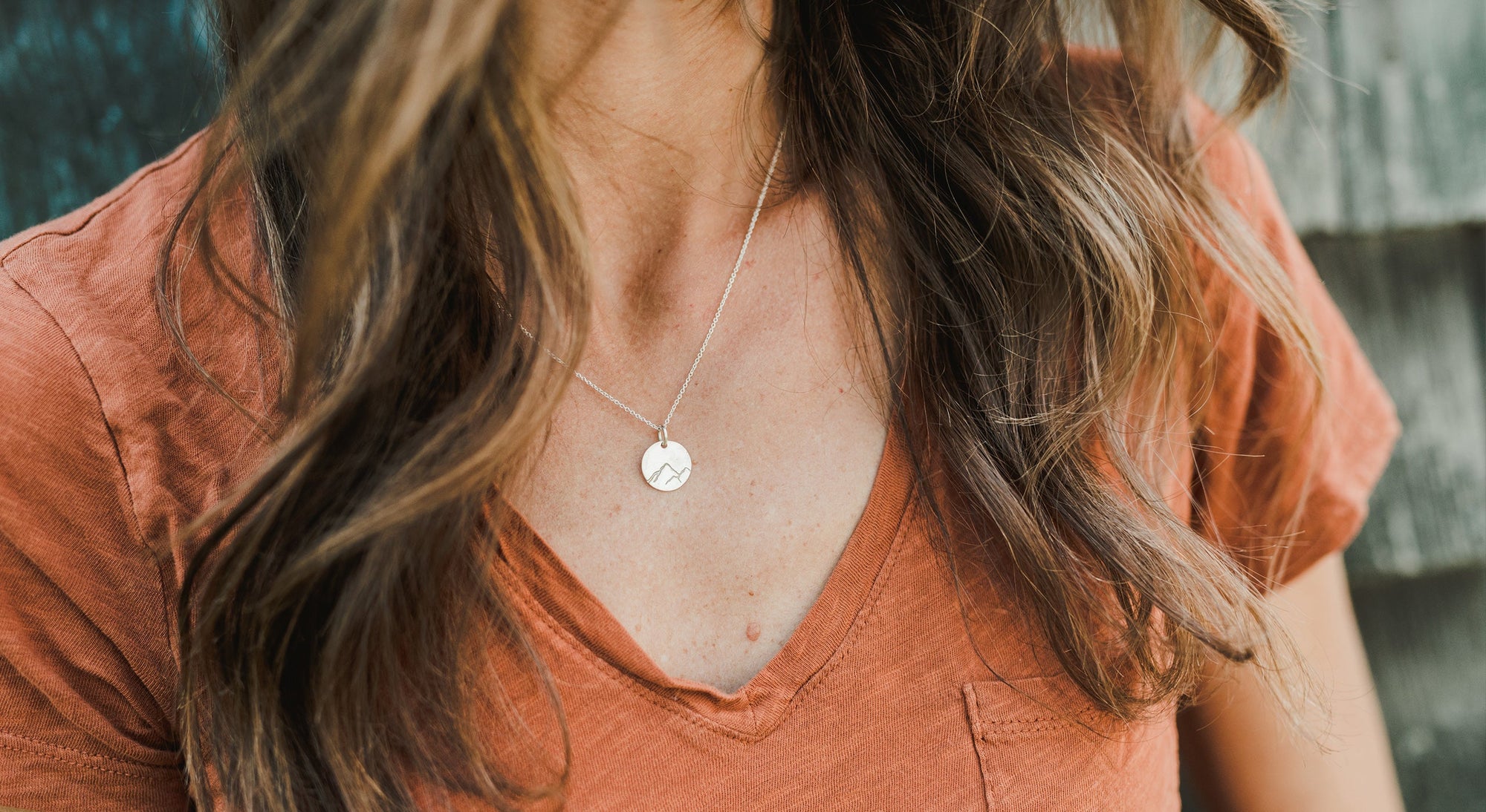 woman in an orange t-shirt wearing a Becoming necklace