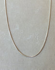 The Becoming Jewelry Box Chain Necklace, with its lightweight, thin silver design, is displayed against a plain, light gray background, offering a classic look.