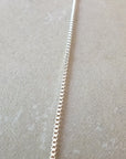 A close-up image of a lightweight, thin silver Box Chain Necklace by Becoming Jewelry laid out on a neutral-toned surface, exuding a classic look.