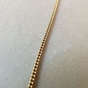 Close-up of a Becoming Jewelry gold-filled curb chain necklace on a light-colored surface.