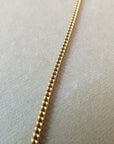 Close-up view of a delicate classic Curb Chain Necklace by Becoming Jewelry lying flat on a beige surface.