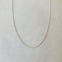A delicate silver Curb Chain Necklace from Becoming Jewelry is displayed on a light grey background, perfect for layering with other necklaces.