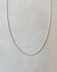 A delicate silver Curb Chain Necklace from Becoming Jewelry is displayed on a light grey background, perfect for layering with other necklaces.