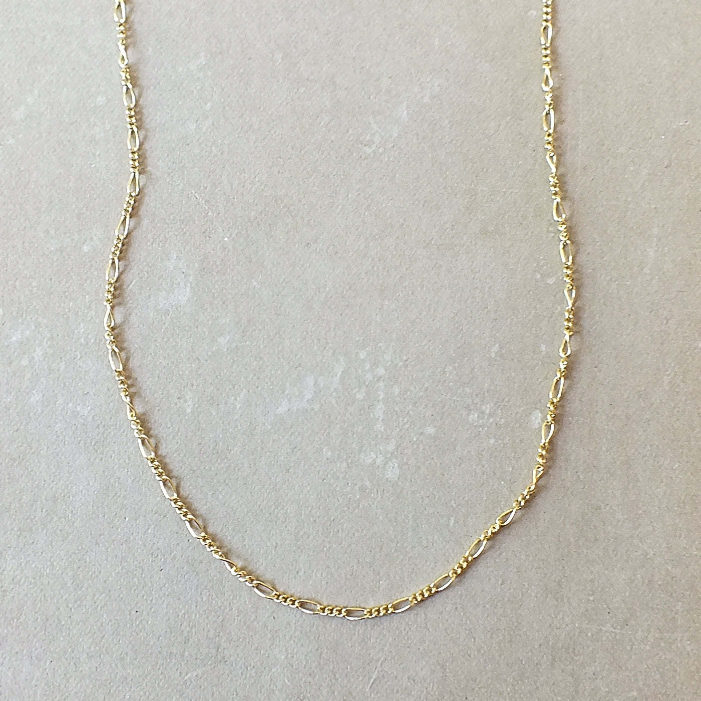 Becoming Jewelry&#39;s Gold Filled Figaro Chain necklace on a neutral background.