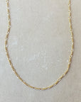 A delicate Becoming Jewelry Figaro Chain Necklace, crafted with small, interlinked oval links, displayed on a light beige surface.