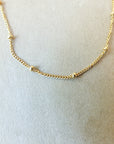 Presenting the Becoming Jewelry Satellite Chain Necklace, adorned with small, evenly spaced beads, elegantly presented on a beige surface. It's an ideal piece for layering to achieve a graceful style or wearing solo as your everyday go-to necklace.