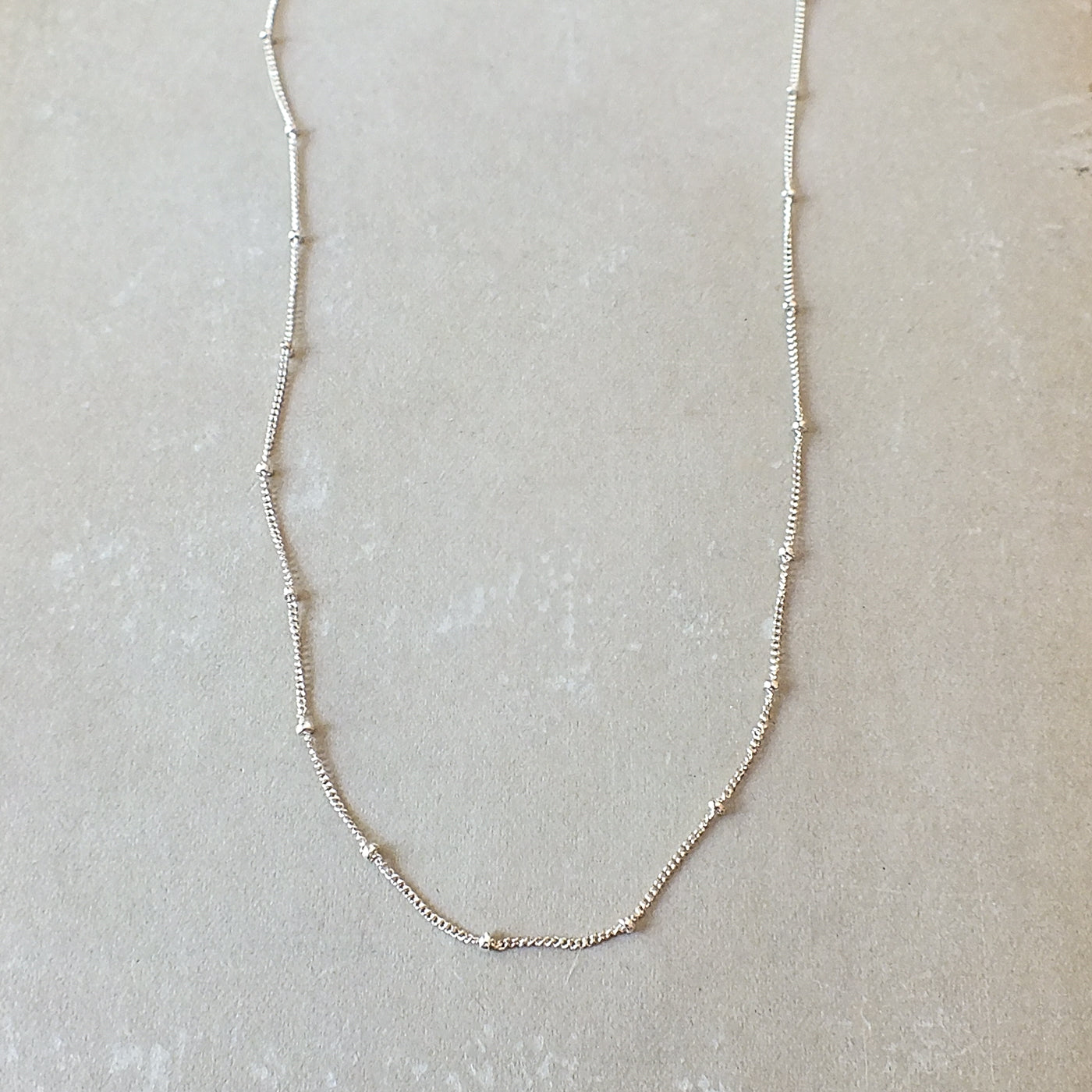 Becoming Jewelry&#39;s sterling silver Satellite Chain Necklace is featured on a gray background.