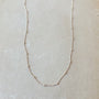 A delicate, thin Satellite Chain Necklace from Becoming Jewelry rests on a light-colored surface, ideal for layering with other necklaces to achieve an everyday look.