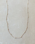 A delicate, thin Satellite Chain Necklace from Becoming Jewelry rests on a light-colored surface, ideal for layering with other necklaces to achieve an everyday look.