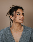 Woman wearing a gray sweater and turquoise beaded necklace against a beige background
