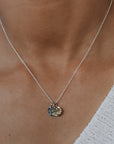 Necklace with a pendant worn by a person in a white sweater.
