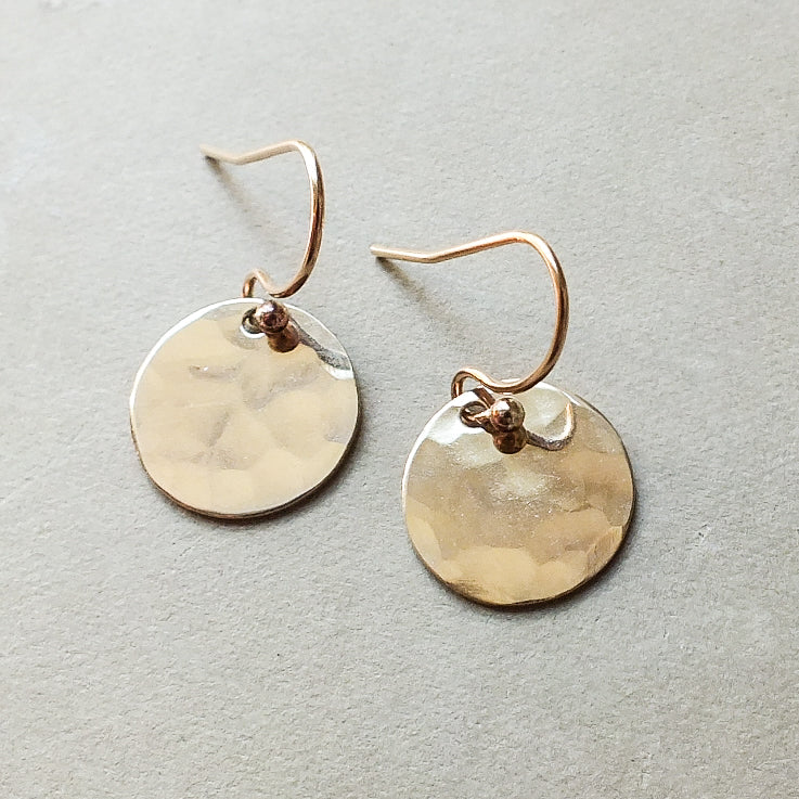 A small pair of Hammered Disc Drop Earrings from Becoming Jewelry, featuring round, hand-hammered gold discs with French hook ear wires, displayed on a neutral surface.