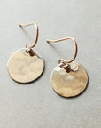 A small pair of Hammered Disc Drop Earrings from Becoming Jewelry, featuring round, hand-hammered gold discs with French hook ear wires, displayed on a neutral surface.