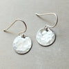 A pair of Becoming Jewelry hammered disc drop earrings with hammered disc drop charms.