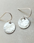 A pair of Becoming Jewelry hammered disc drop earrings with hammered disc drop charms.