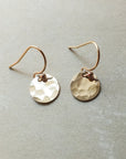 A pair of tiny Hammered Disc Drop Earrings handcrafted from gold by Becoming Jewelry, featuring lightweight discs and simple hooks, showcased on a flat, neutral background—ideal for everyday wear.