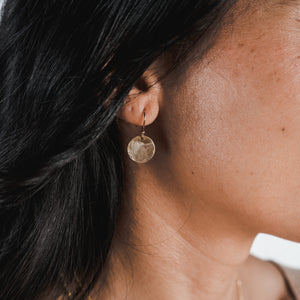A close-up of a woman wearing Becoming Jewelry's small Hammered Disc Drop Earrings.