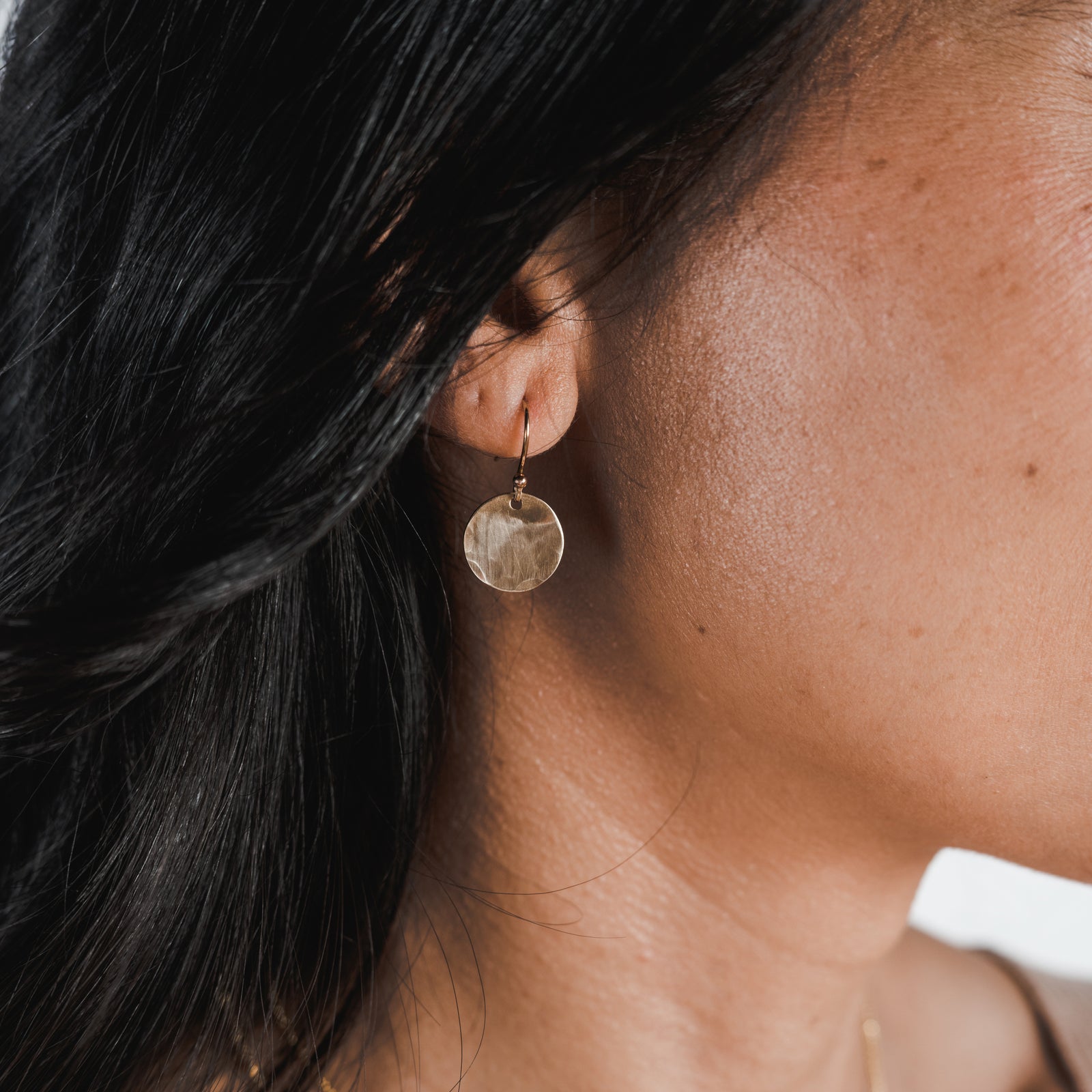 A close-up of a woman wearing Becoming Jewelry's small Hammered Disc Drop Earrings.