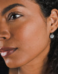 Profile view of a woman with curly hair wearing Becoming Jewelry's Tiny Hammered Disc Drop Earrings.