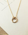 Close-up of the exquisite Family Circle Necklace by Becoming Jewelry, showcasing a pendant with three interlocking rings symbolizing strength and love, displayed on a textured white surface. This beautiful piece makes the perfect go-to gift.
