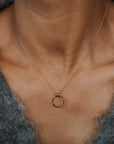 Gold necklace with a small ring pendant on a person wearing a gray sweater.