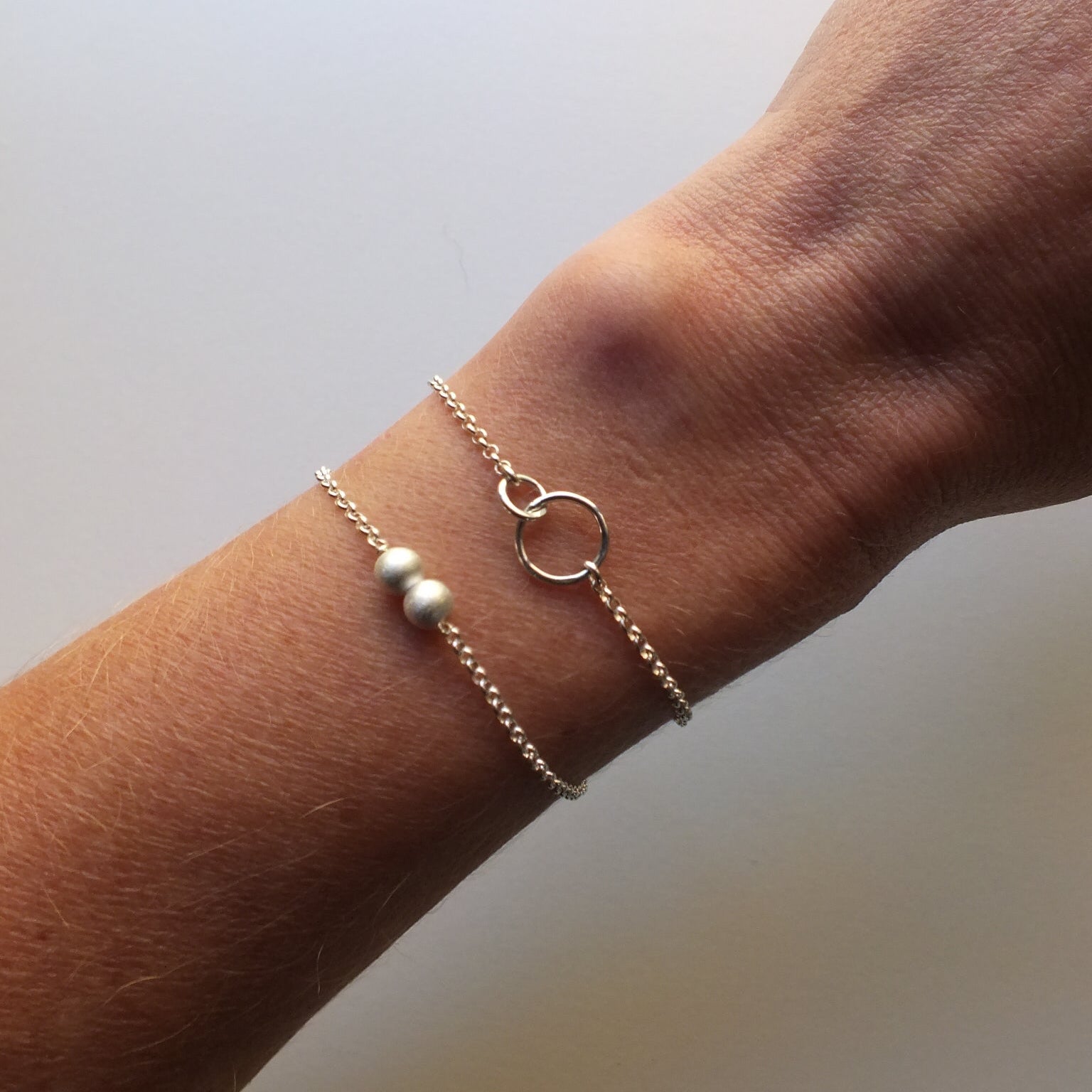 Close-up of a wrist wearing two bracelets on a plain background