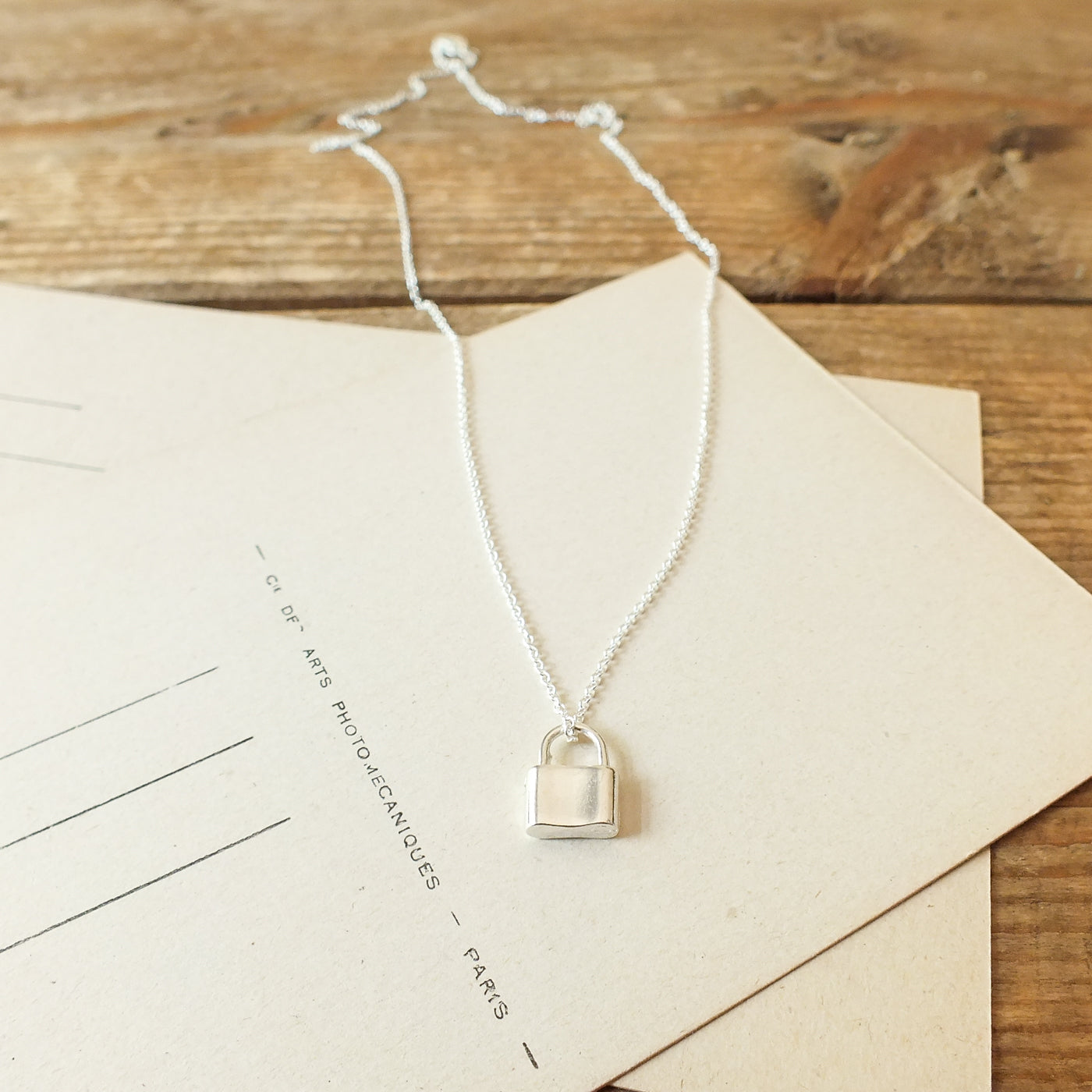 Hidden Treasures Necklace by Becoming Jewelry with a padlock pendant displayed on a beige card.