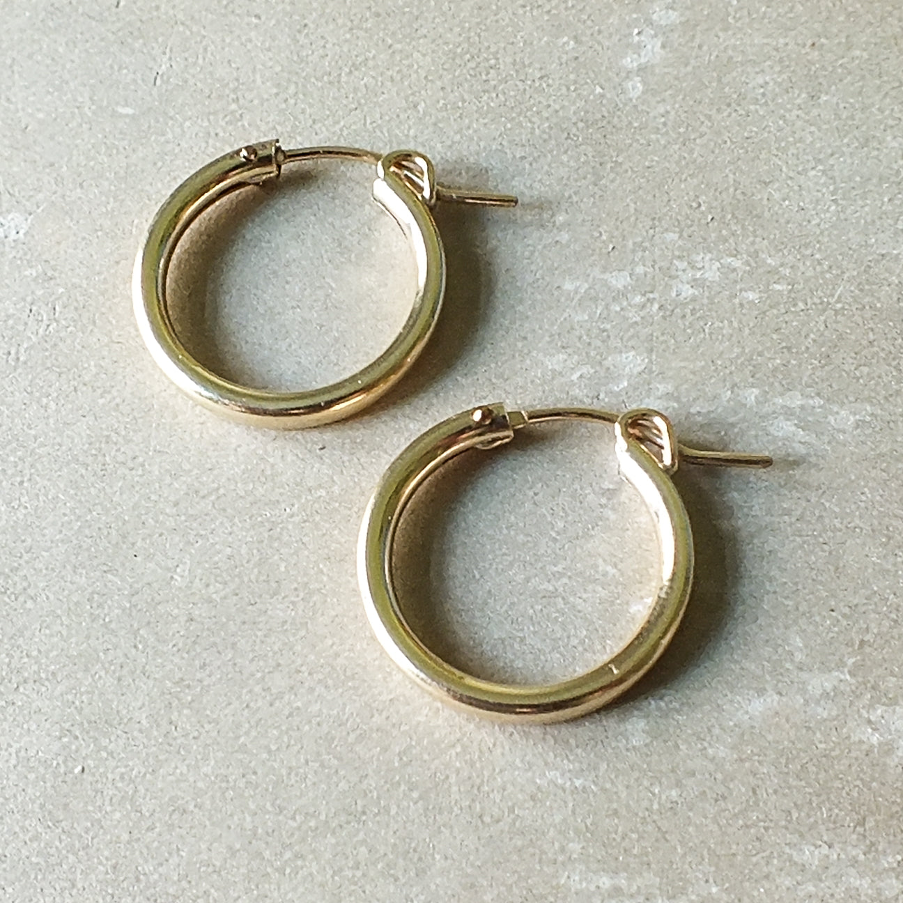 A pair of classic large gold hoop earrings from Becoming Jewelry's Everyday Hoop Earrings collection, elegantly displayed on a beige surface—perfect for everyday wear.