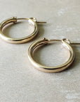 Close-up of a pair of large, classic gold Everyday Hoop Earrings from Becoming Jewelry on a light beige surface, perfect for everyday wear.