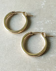 A pair of classic large gold hoop earrings from Becoming Jewelry's Everyday Hoop Earrings collection, elegantly displayed on a beige surface—perfect for everyday wear.