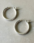 Two large silver hoop earrings from Becoming Jewelry, perfect for everyday wear, are elegantly placed on a beige surface.