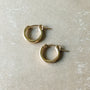 A pair of Becoming Jewelry's Everyday Hoop Earrings, in a small size and classic lightweight gold design, lying on a beige surface—perfect for everyday wear.