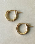 A pair of Becoming Jewelry Everyday Hoop Earrings, small on a grey surface.
