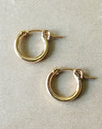 A pair of Becoming Jewelry's Everyday Hoop Earrings, small, lying on a light grey surface perfect for everyday wear.